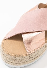 Růžové semišové a metalické růžově zlaté espadrilky s křížovým páskem, přírodní pletenou juteovou mezipodešví a gumovou podešví. Viditelné texturované materiály.