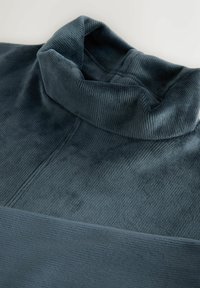 Sötét szürke bordázott fleece anyag, hajtott magas gallérral, világos háttér előtt bemutatva.