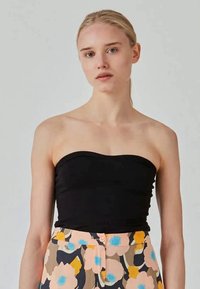 Black strapless top made of smooth fabric, featuring a fitted design. Paired with floral-patterned pants in pastel colors, including orange and blue.