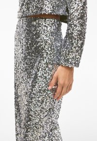 Silverglittrande paljettoutfit med en kort topp och en figursydd kjol. Slät textur med glänsande cirkulära paljetter som reflekterar ljus.