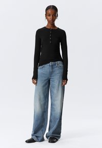 Svart langermet topp med knappedetaljer, kombinert med lyseblå, vide jeans. Jeansen har en falmet tekstur og en avslappet passform.