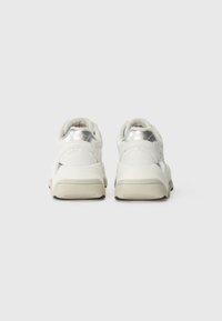 Sneaker bianchi con accenti argentati, tomaia testurizzata, collo imbottito e suola chunky beige. Design minimalista con superfici lisce.