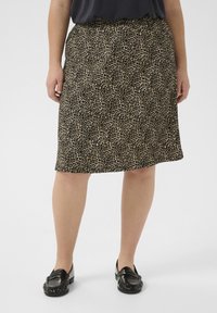 Jupe en tissu imprimé léopard beige et noir, dotée d'une taille élastique et d'une coupe droite. Associée à des mocassins noirs.