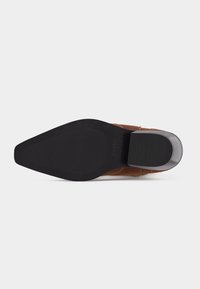 Semelle de botte de cow-boy en cuir noire avec bout pointu et talon empilé, vue de dessous sur fond blanc.