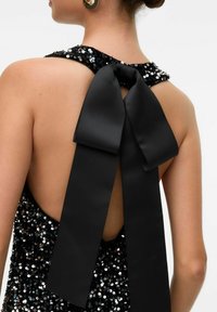 Juoda blizgučių suknelė su atvira nugarėle, su dideliu juodu satino kaspinu ant kaklo. Lygi tekstūra, atspindintys blizgučiai ir dekoratyvūs akcentai.