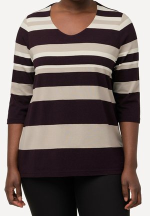 Femme portant un haut à manches trois-quarts avec de larges rayures horizontales noires, beiges et blanc cassé, associé à un pantalon noir.
