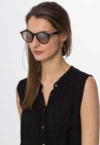 Ochelari de soare rotunzi, negri, cu lentile fumurii, având un cadru subțire. Purtașul are păr lung și drept și este îmbrăcat cu un top negru fără mâneci.