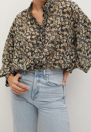 Femme portant un chemisier noir à fleurs à manches longues avec col volanté et un jean taille haute bleu clair, mains près des poches.