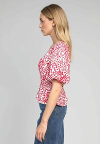 Blouse rouge et blanche avec des manches courtes bouffantes, une taille froncée et un motif à pois. Associée à un jean bleu, affichant une coupe décontractée.
