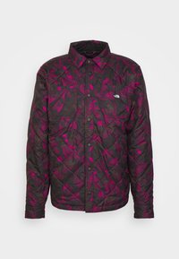 Vadderad jacka i svart med ett lila växtmönster, med knäppning fram, två bröstfickor och en krage.