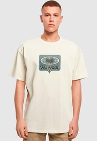 Krēmkrāsas kokvilnas t-krekls ar grafiku, kurā attēlots globuss un uzraksts "wu wear". Īsas piedurknes, brīvs griezums, mīksta tekstūra.