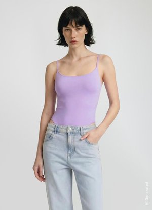 Giovane donna con capelli neri corti che indossa un top color lavanda con spalline sottili e jeans azzurri chiari, in piedi con una mano in tasca.