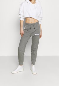 Witte cropped hoodie met een trekkoord, gecombineerd met grijze sweatpants met zijzakken en "CALVIN KLEIN" merkopdruk in het wit. Witte sneakers.