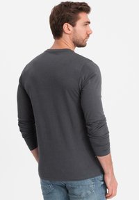 Graues Langarm-T-Shirt aus weichem Baumwollstoff. Verfügt über einen runden Ausschnitt und figurbetonte Ärmel, kombiniert mit hellblauen Jeans.