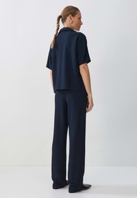 Haut à manches courtes bleu marine et pantalon large en tissu lisse. L'ensemble présente un ourlet droit et une coupe décontractée, avec un minimum de détails.