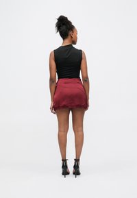 Top negro sin mangas, falda corta burdeos con ribete de encaje, tela texturizada y zapatos negros de tacón alto. Vista desde atrás.