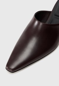 Mule a punta in pelle marrone scuro con una texture liscia e un design minimalista, caratterizzate da un retro aperto e una silhouette elegante.