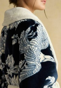 Námornícky modrý župan s jemným krémovým golierom; obsahuje zložitých bielych vzorov vtákov a kvetov, vyrobený zo zamatového materiálu.