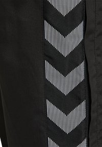 Svart plagg med en vertikal panel av svart och vitrandig tyg med zigzag-mönster. Texturen verkar slät och elegant.