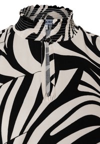 Schwarz-weiße Bluse mit Muster, hohem, gerafftem Kragen, Schlitz an der Vorderseite und Knopfdetail am Kragen. Glatte Stoffstruktur.