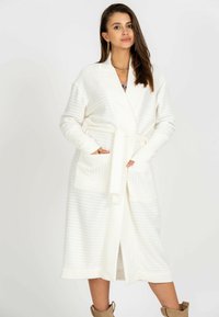 Biała żebrowana długa szata z pasek do wiązania, dwoma przednimi kieszeniami i długimi rękawami. Miękka faktura zapewnia ciepło i komfort.