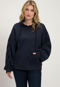 Marineblauwe oversized hoodie gemaakt van zachte stof, met een grote voorzak, een capuchon met trekkoord en opgeblazen mouwen met geribde manchetten.
