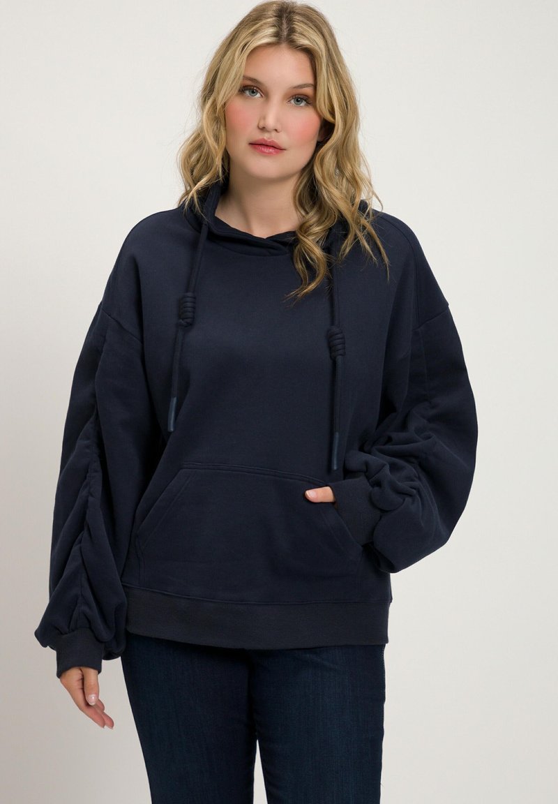 Marineblauwe oversized hoodie gemaakt van zachte stof, met een grote voorzak, een capuchon met trekkoord en opgeblazen mouwen met geribde manchetten.