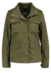 Kurtka militarna w kolorze oliwkowej zieleni wykonana z bawełny, z wysokim kołnierzem, wieloma przednimi kieszeniami i zapięciami na zatrzaski.