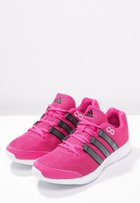 Zapatillas deportivas rosas con parte superior de malla, rayas grises y suelas blancas. Presentan cordones contrastantes y logotipo en la lengüeta.