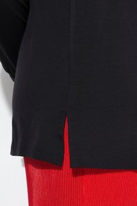 Schwarzes Baumwolloberteil mit einem Seitenschlitz, kombiniert mit roten gerippten Leggings. Das Oberteil hat ein schlichtes Design und eine glatte Textur.