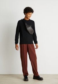 Black sweater, relaxed maroon pants, and a brown patterned crossbody bag. Black shoes with yellow stitching. Light background.