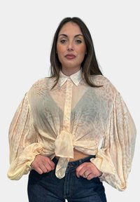 Blusa leggera e trasparente color pesca con stampa leopardata, colletto abbottonato e maniche a sbuffo voluminose, legata davanti su jeans blu scuro.