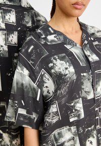 Camicia a maniche corte bianco e nero con un collage di stampe fotografiche, con un design a bottoni e una texture di tessuto liscia.