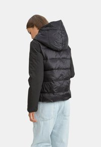 Czarna kurtka puchowa z kapturem, wykonana z błyszczącego materiału na górze i matowej tkaniny na rękawach, z detalicznym przeszyciem na plecach.