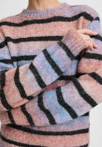 Pull en tricot aux couleurs pastel avec des rayures noires, présentant un col rond et des poignets côtelés. Texture douce, coupe légèrement surdimensionnée.