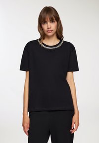 T-shirt nera con scollatura rotonda decorata con perline metalliche. Maniche corte e taglio comodo.