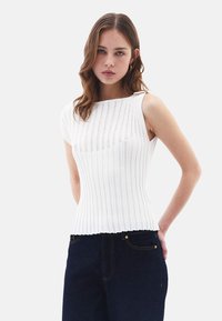 Vit ribbad ärmlös topp med vertikala ränder, med båturringning och textilier med struktur. Matchad med mörkblå jeans.