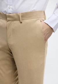 Pantaloni bej, croiți, cu o textură netedă, croi slim, buzunare laterale și talie standard cu bucle pentru curea.