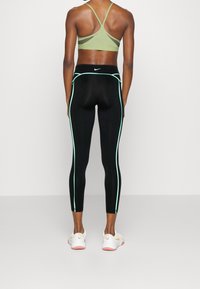 Czarne legginsy z turkusowymi paskami po bokach, zestawione z jasnoszarym biustonoszem sportowym. Buty są białe z różowymi akcentami. Skupienie na projekcie odzieży sportowej.