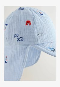Gorra de algodón azul claro con motivos marinos bordados, incluyendo peces y un cangrejo, con visera curva y tela texturizada.