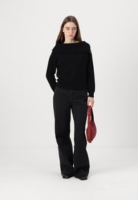 Juodas megztinis su off-shoulder dizainu, derinamas su aukštu iškeltu juodu flared džinsų modeliu. Raudona kreivėta rankinė užbaigia įvaizdį.