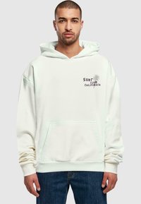 Cream-colored hoodie made of soft cotton, featuring a front pocket, ribbed cuffs, and "SURF CLUB CALIFORNIA" graphic with palm tree design.