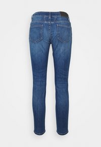 Blue slim-fit denim jeans shown from the back with two back pockets and a brown leather brand patch on the waistband.