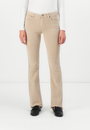 Beige corduroy broek met rechte pijpen, gedragen met een wit shirt met lange mouwen en zwarte veterschoenen op een witte achtergrond.