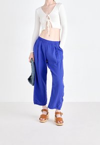 Pantalon bleu léger à jambes larges en tissu texturé, taille élastique et poches latérales, associé à un haut court blanc côtelé et des sandales à talons en bois.