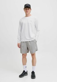 Witte longsleeve shirt met een logo, grijze shorts, zwarte sportschoenen en een zwarte pet. Glad materiaal en een relaxte pasvorm.