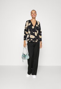Top avvolgente nero e beige con motivo, scollatura a V, maniche lunghe e dettaglio con laccio, abbinato a pantaloni larghi neri e sneaker bianche.