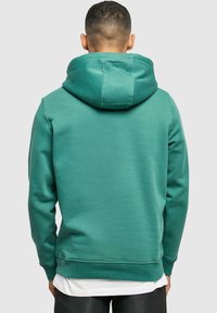 Zielona bluza z kapturem wykonana z miękkiego materiału, z dużym kapturem, długimi rękawami i ściągaczem u dołu. Minimalistyczny design, bez widocznych wzorów czy akcentów.