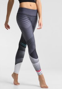 Dopasowane legginsy w geometryczny wzór, głównie szare z akcentami bieli, turkusu i różu. Posiadają szeroką talię.