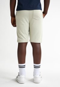 Lichtgroene, knielange shorts van zachte stof, met een achterzak en een ontspannen pasvorm, gecombineerd met witte sokken en sneakers.